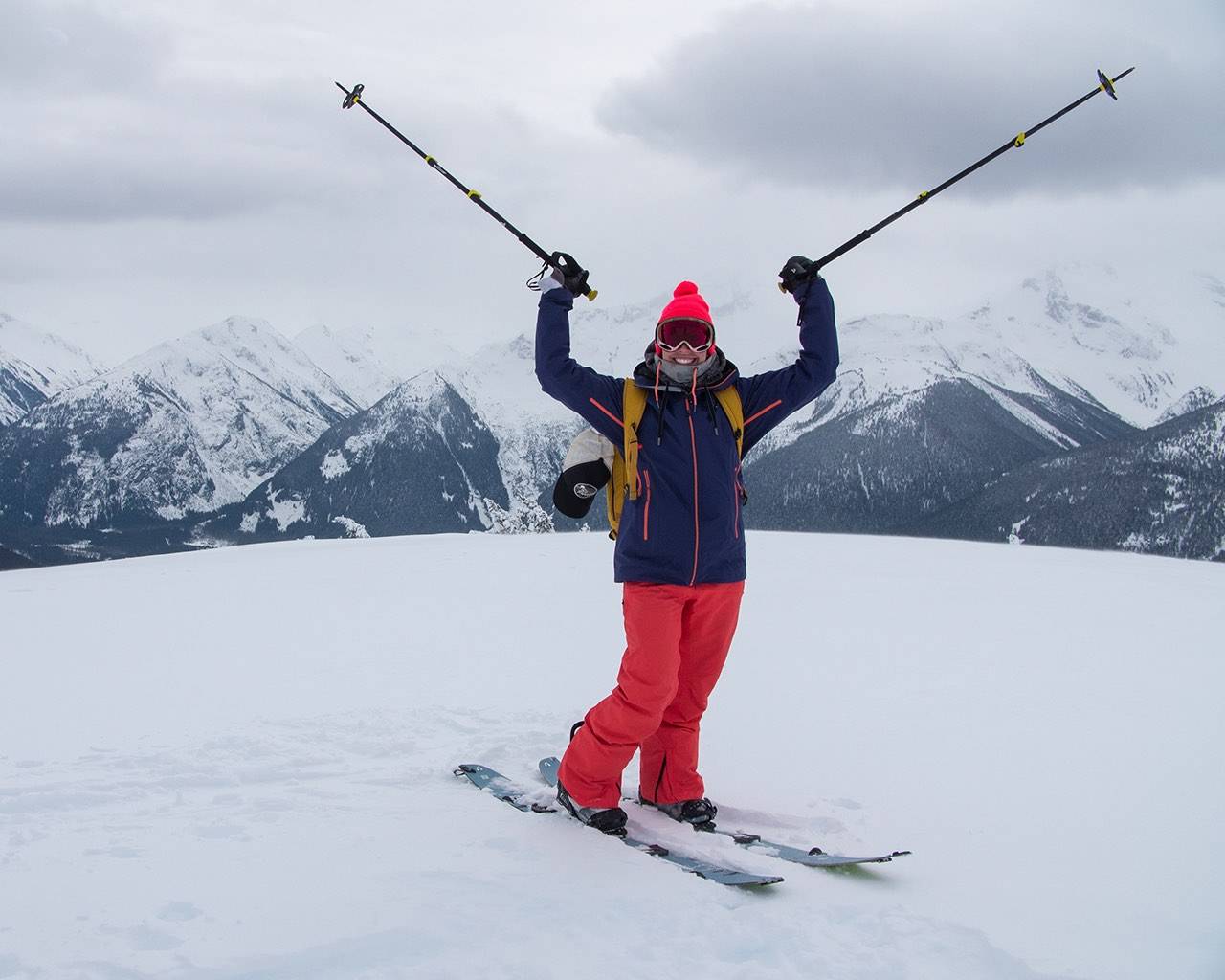 Woman smiling stood atop a peak backcountry skiing
